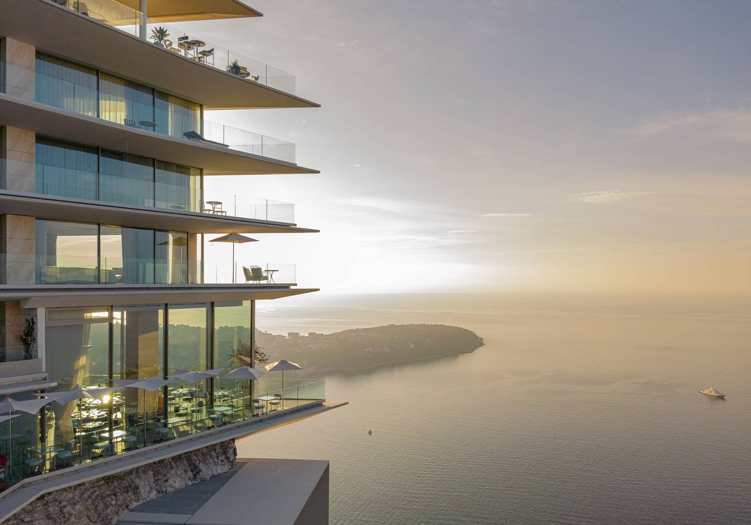 A stunning modern building with glass balconies overlooking a serene coastal view at sunset.