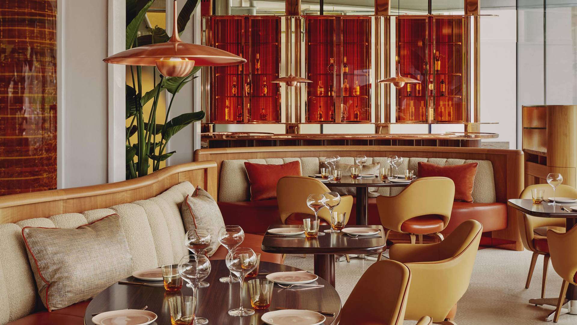 A sophisticated dining area with warm, earthy tones, featuring plush seating, polished tables, and elegant glassware. Ambient lighting and rich red accents create an inviting, upscale atmosphere.