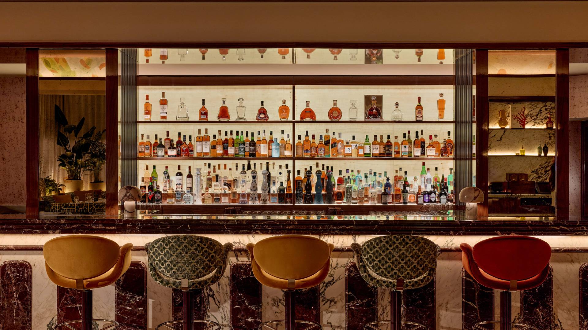 Sophisticated bar with a marble counter and a colourful selection of spirits on backlit shelves.