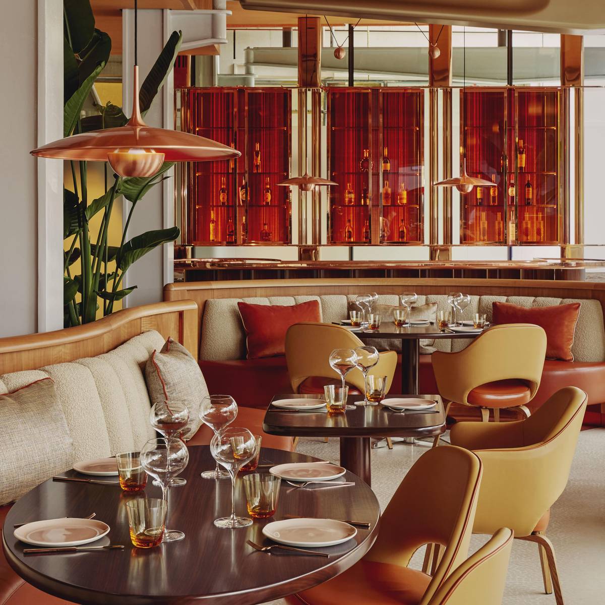 A sophisticated dining area with warm, earthy tones, featuring plush seating, polished tables, and elegant glassware. Ambient lighting and rich red accents create an inviting, upscale atmosphere.