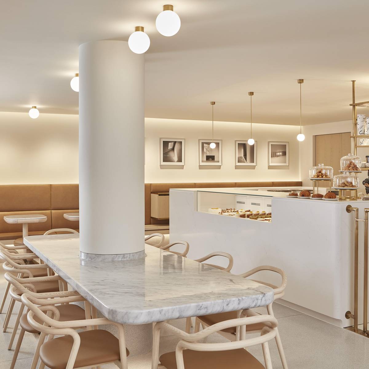 A serene café with marble tables, warm leather seating, and a pastry counter, elegantly lit by spherical pendant lights.