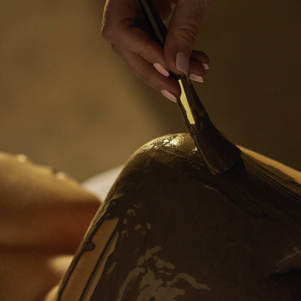 A luxurious body treatment in progress, with a therapist carefully applying a rich mud mask to the client's shoulder, promoting relaxation and rejuvenation