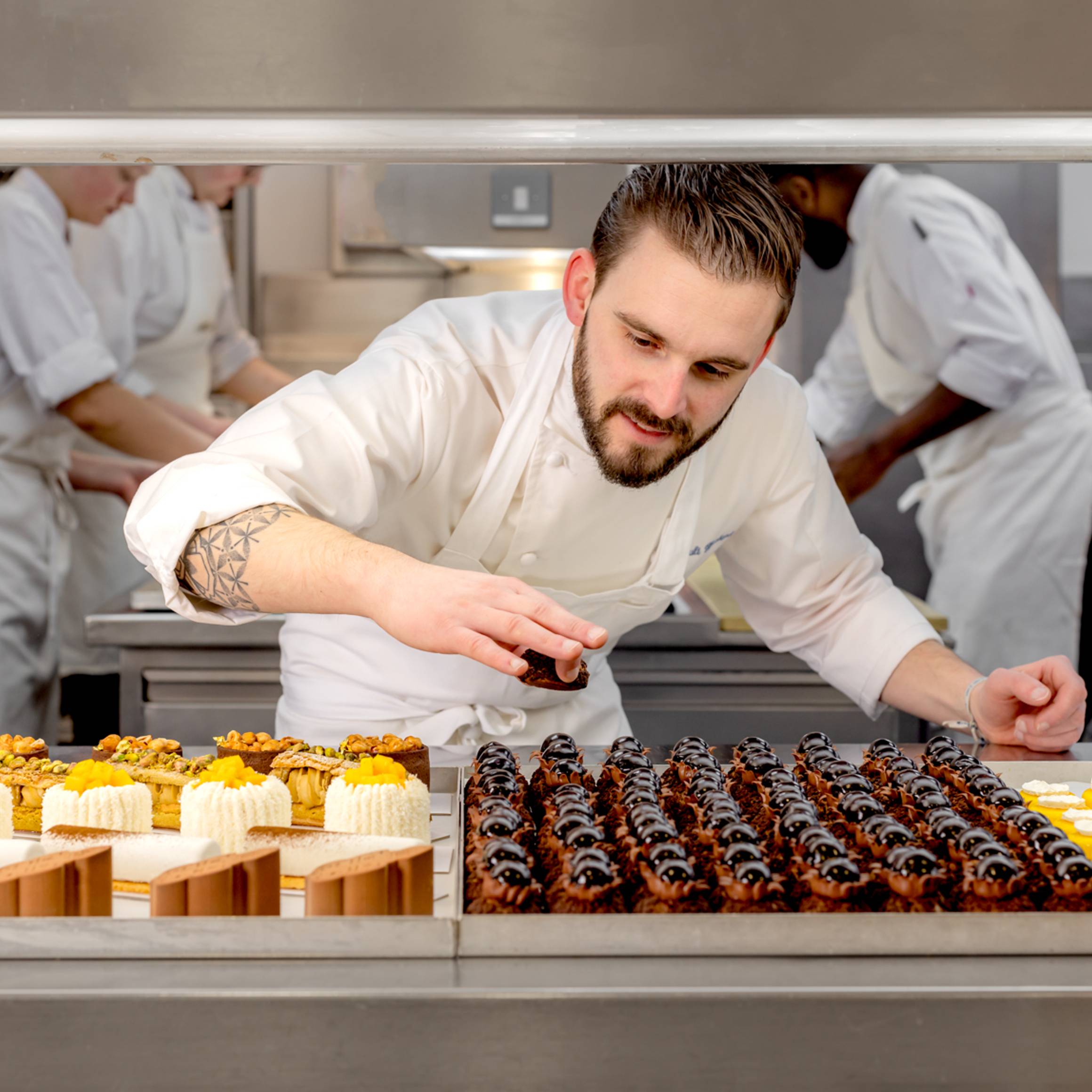 A pastry chef carefully places finishing touches on exquisite desserts in a bustling, professional kitchen.
