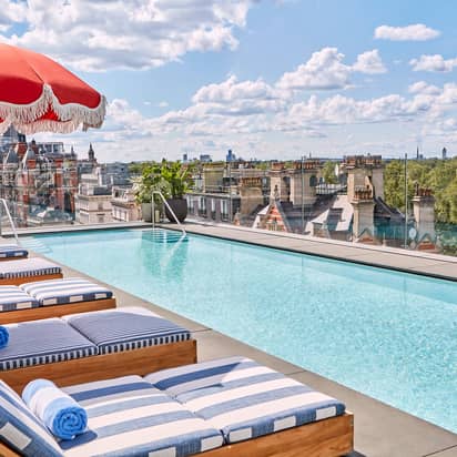 Rooftop pool with striped loungers, red parasols, and skyline views over London and Hyde Park.