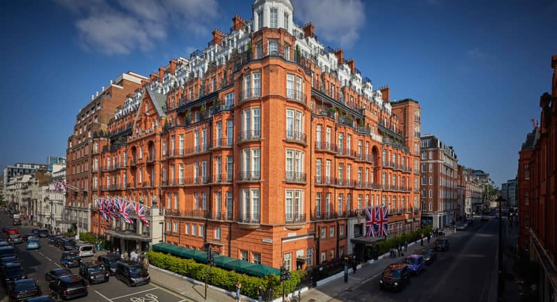 The grand red-brick facade of Claridge’s Hotel in Mayfair, adorned with Union Jack flags and intricate architectural details.