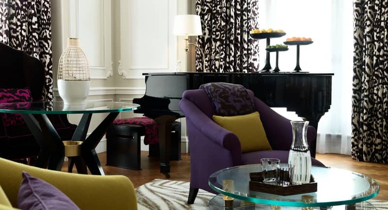 A stylish suite with vibrant furnishings, a grand piano, and sophisticated decor in a spacious, light-filled setting.