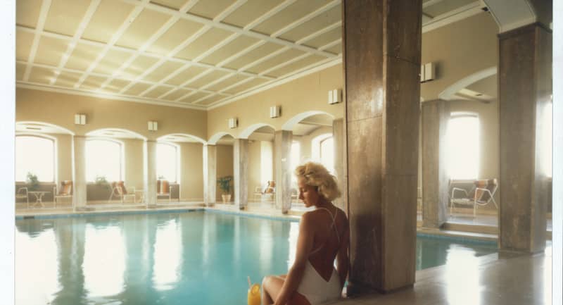 Serene indoor pool scene at The Berkeley, featuring a woman in a white swimsuit seated poolside with a refreshing drink