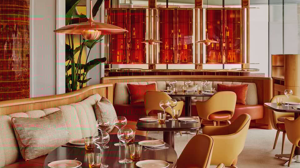 Contemporary dining space with warm tones, curved seating, stylish pendant lights, and vibrant red accents creating a modern ambiance.