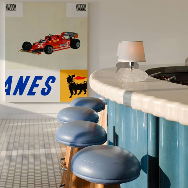 Retro-inspired bar with a curved marble countertop, blue leather stools, and bold artwork featuring a classic race car.