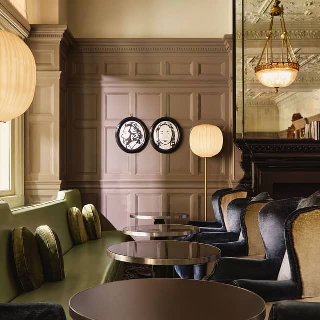 Sophisticated lounge with green and velvet seating, contemporary portraits, and ornate ceiling details reflecting timeless elegance