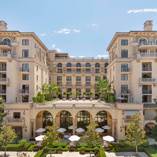Courtyard view of The Maybourne Beverly Hills, featuring elegant arches, lush greenery, and stylish balconies under a clear sky