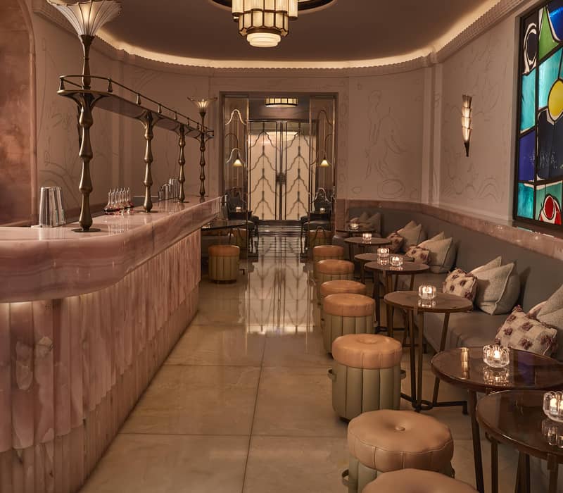 Art Deco-inspired bar with a pink marble counter, plush seating, stained glass accents, and warm ambient lighting.