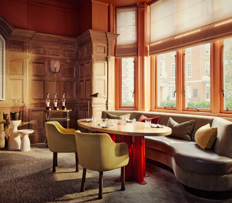 Warm, inviting dining space with wood-paneled walls, large sunlit windows, curved seating, and elegant decor creating a cosy ambiance.