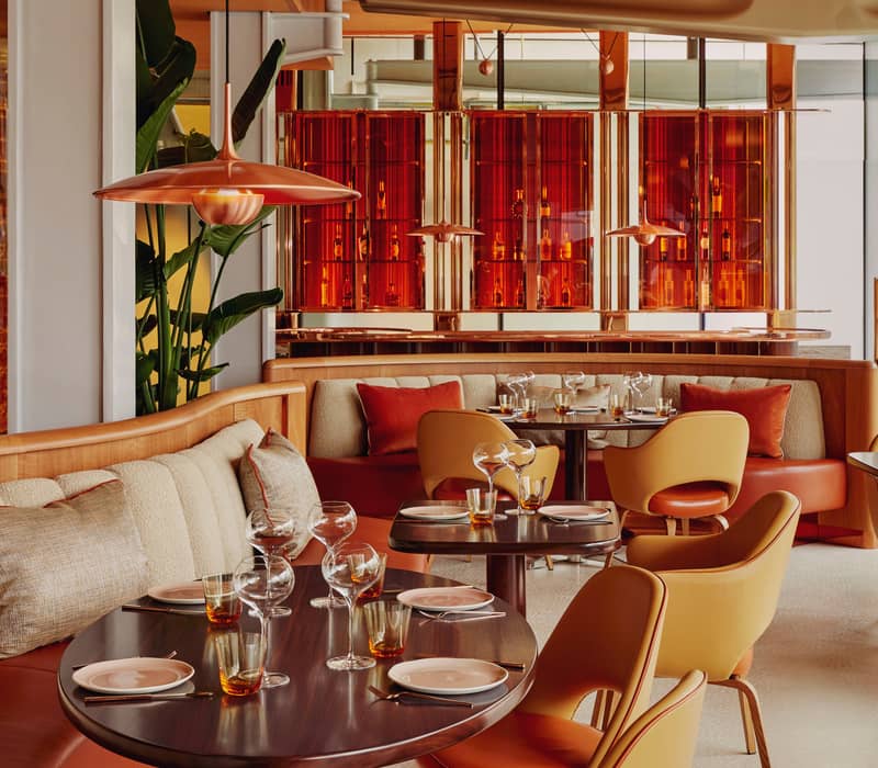 Contemporary dining space with warm tones, curved seating, stylish pendant lights, and vibrant red accents creating a modern ambiance.
