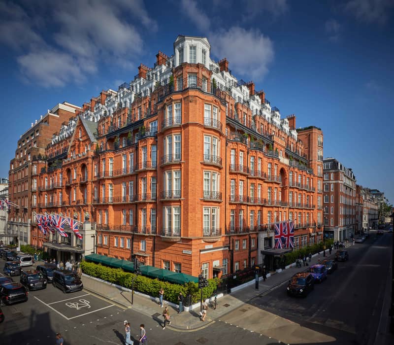 The grand red-brick facade of Claridge’s Hotel in Mayfair, adorned with Union Jack flags and intricate architectural details.