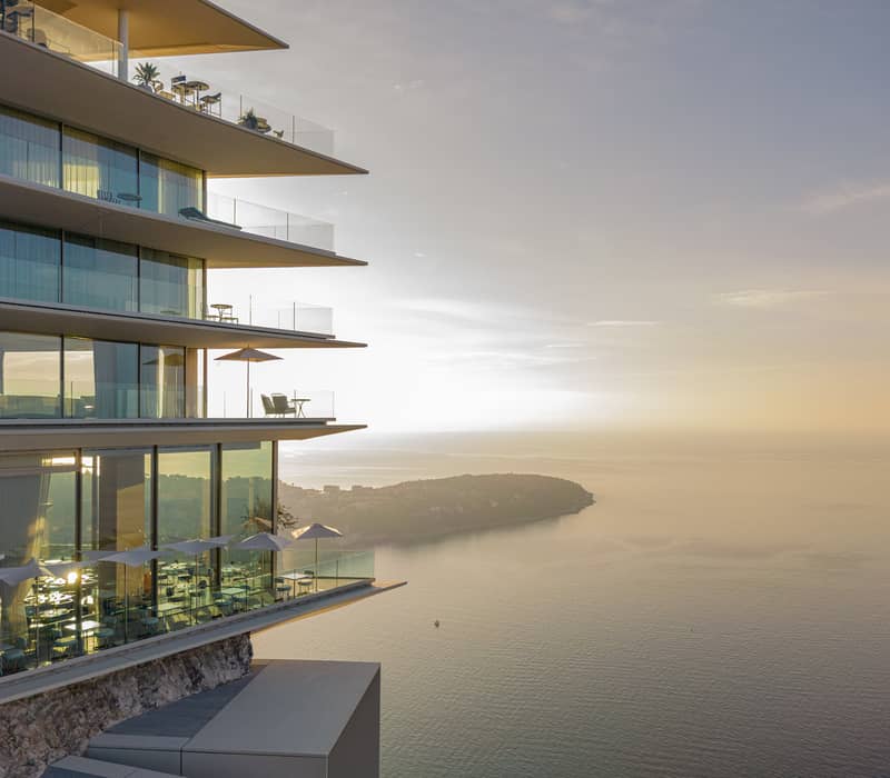 A stunning modern building with glass balconies overlooking a serene coastal view at sunset.