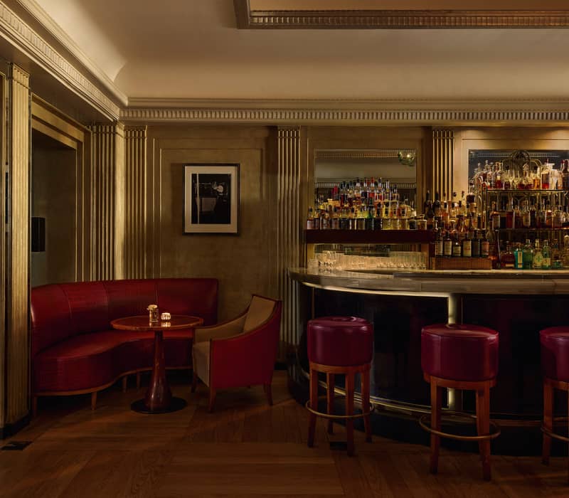 Art Deco-inspired bar with gold accents, crimson seating, and a curved bar lined with premium spirits under soft lighting