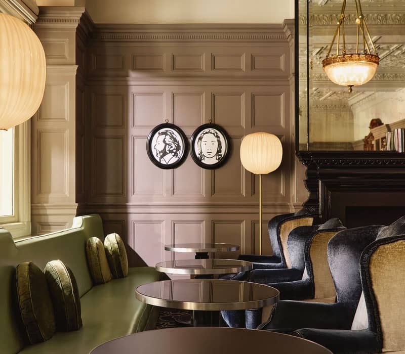 Sophisticated lounge with green and velvet seating, contemporary portraits, and ornate ceiling details reflecting timeless elegance