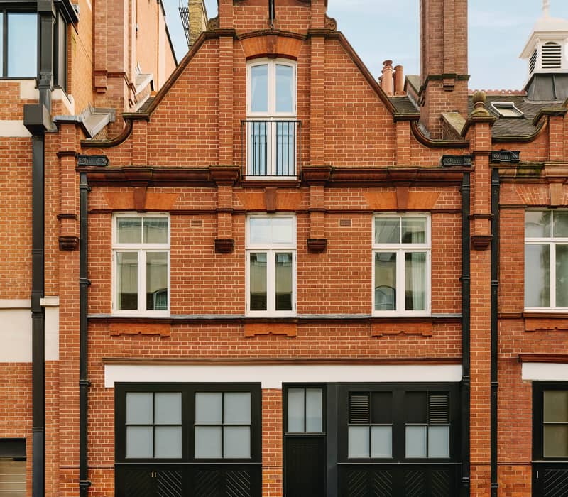 A red-brick townhouse with black garage doors, white-framed windows, and decorative topiary in a serene courtyard.