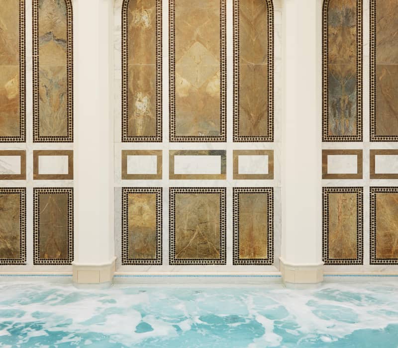 Elegant indoor spa pool with ornate arched wall panels, soothing turquoise water, and skylights creating a serene atmosphere