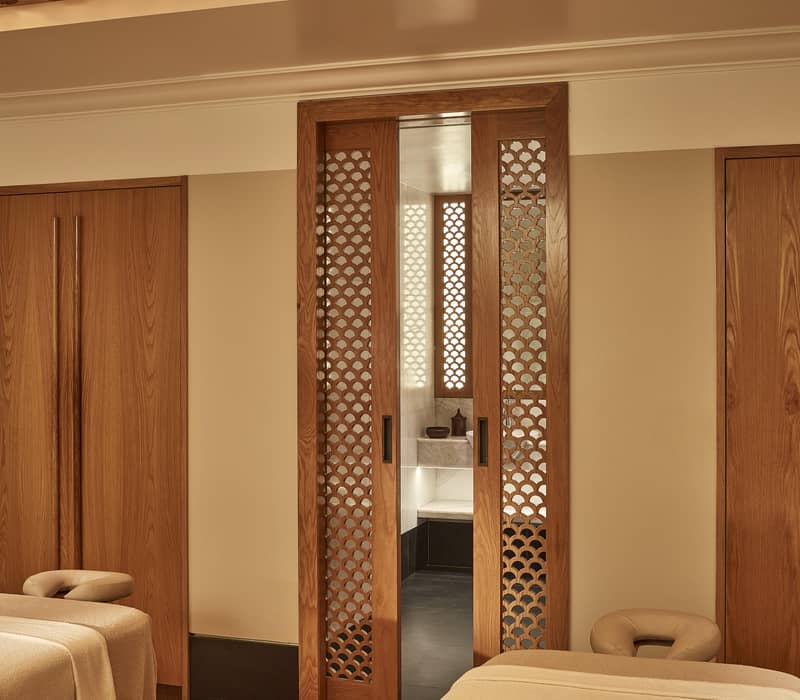 A serene spa room with two massage beds, soft lighting, and wooden sliding doors with intricate patterns for a tranquil ambience.