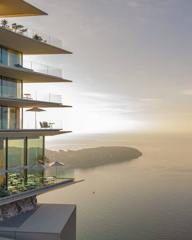 A stunning modern building with glass balconies overlooking a serene coastal view at sunset.