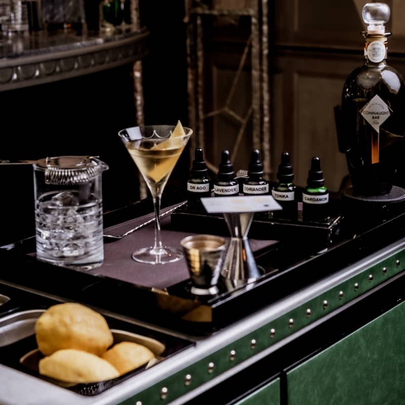 Elegant cocktail trolley with martini, citrus, bitters, and bar tools in a dimly lit luxury setting.