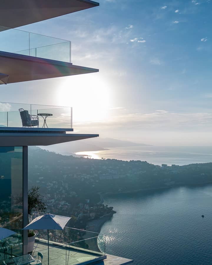 A striking modern building with glass balconies overlooking the coastline, bathed in golden sunlight at sunset.