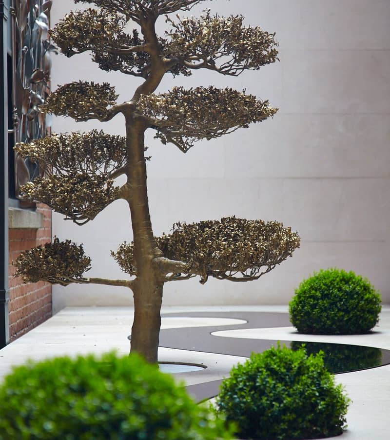 A sculptural bronze tree in a contemporary courtyard, blending art and nature with minimalist landscaping and organic form