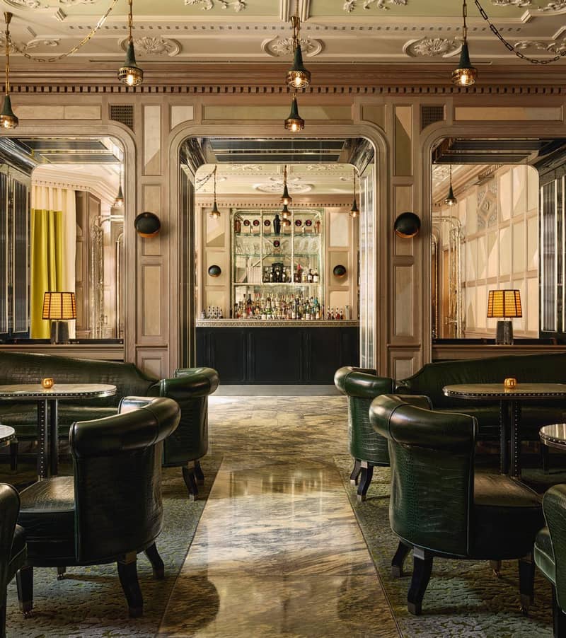 An elegant bar with dark green leather seating, marble floors, mirrored panels, and soft lighting, creating a refined, intimate ambiance.