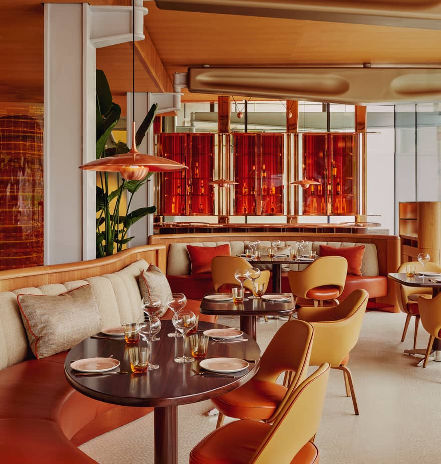 Stylish restaurant with curved banquettes, orange leather chairs, and a striking amber glass bar backdrop.