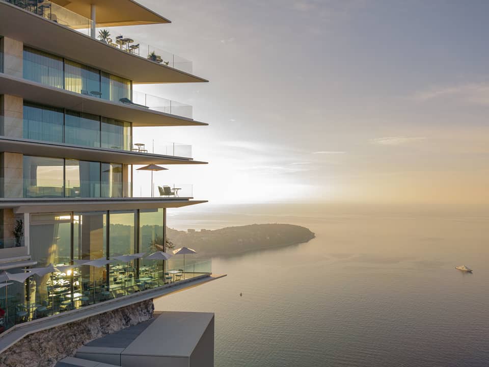 A stunning modern building with glass balconies overlooking a serene coastal view at sunset.