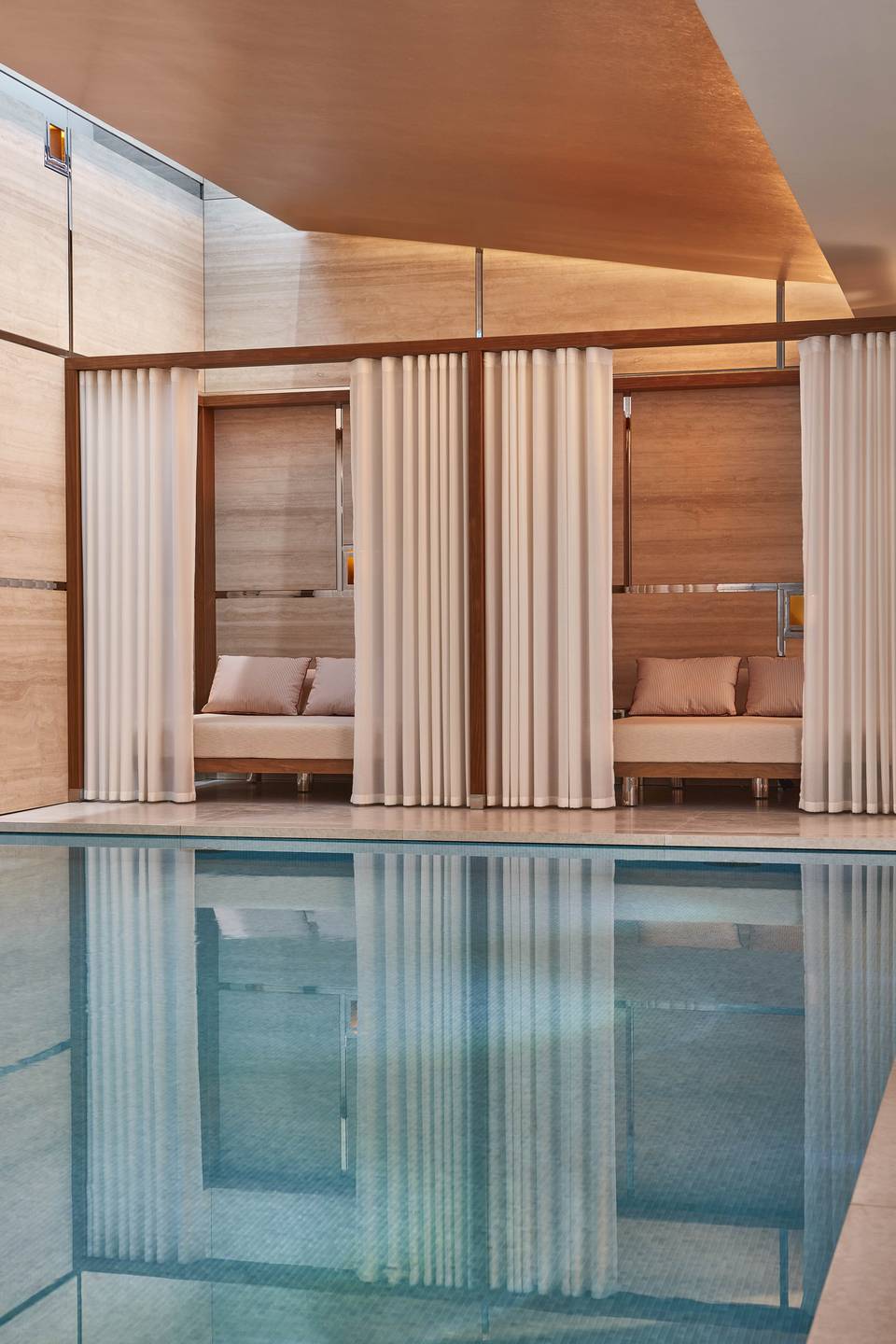 Elegant poolside cabanas with sheer curtains and plush seating, surrounded by warm wood tones, offering a serene, private oasis.
