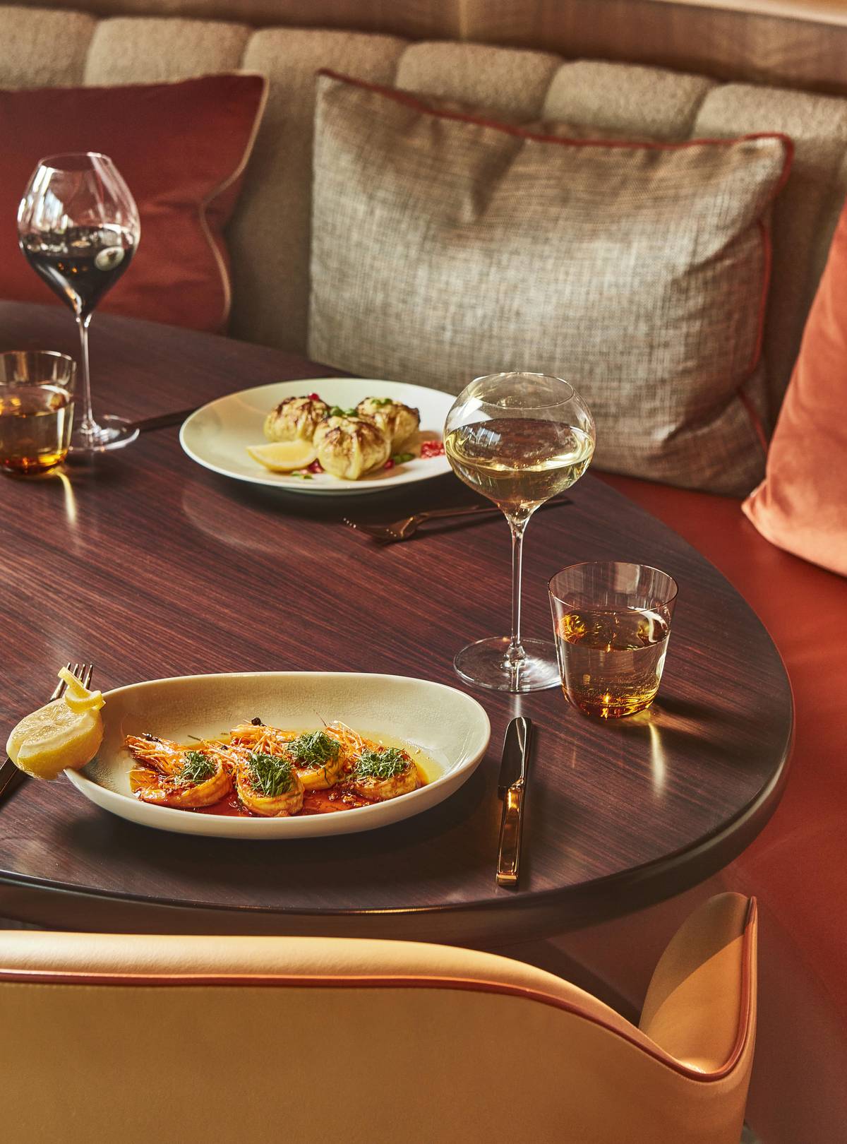 A cozy restaurant setting with plush seating, elegantly plated dishes, and wine glasses, creating a warm, inviting atmosphere.
