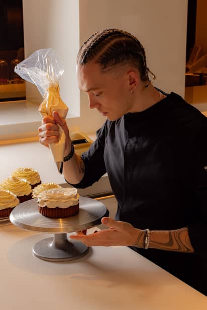 A focused pastry chef piping cream onto a tart, showcasing intricate craftsmanship in a modern kitchen setting.
