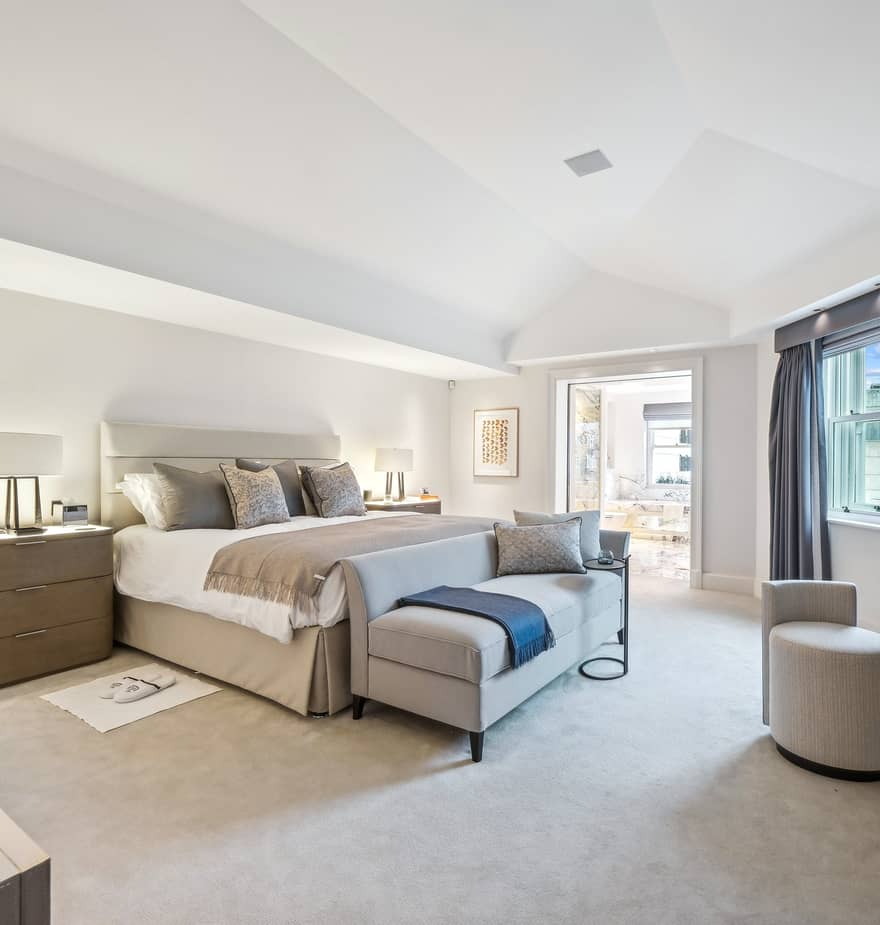 Spacious bedroom with king-size bed, neutral tones, vaulted ceiling, desk, and large windows with natural light.