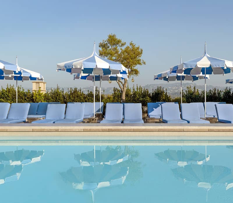 Serene rooftop pool with plush blue loungers, striped umbrellas, and breathtaking views, offering an oasis of relaxation under the sun.