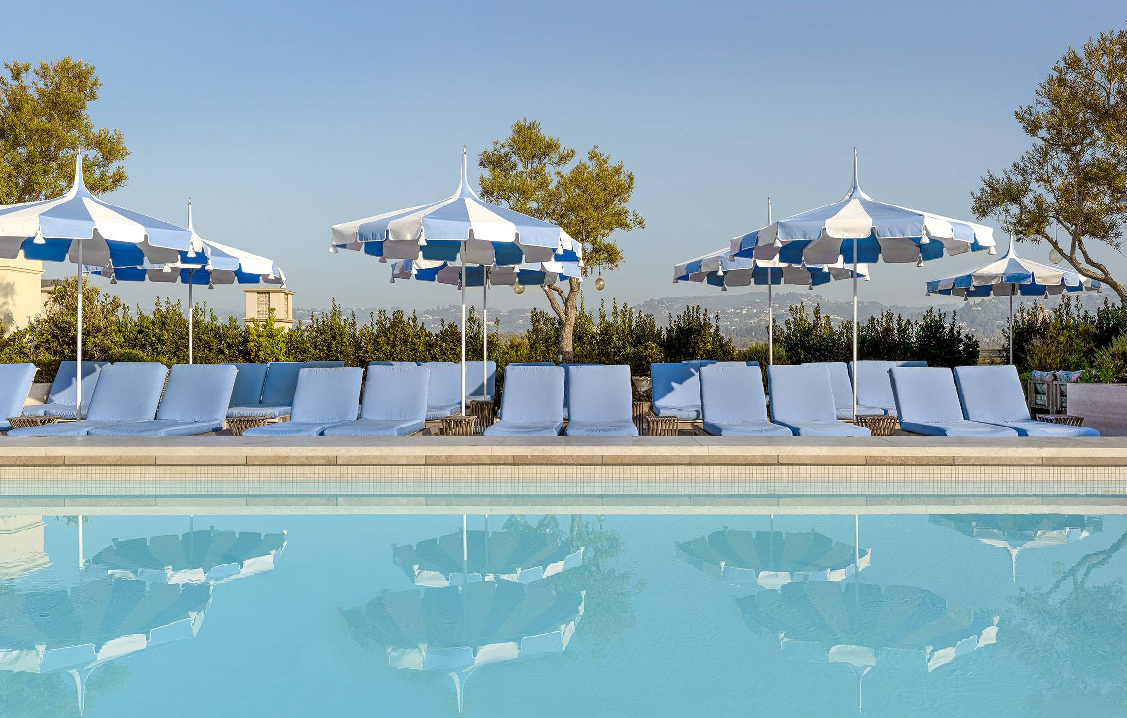 Serene rooftop pool with plush blue loungers, striped umbrellas, and breathtaking views, offering an oasis of relaxation under the sun.