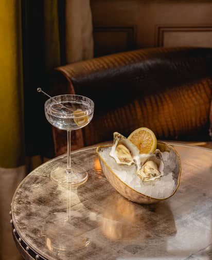 Fresh oysters on ice with lemon, accompanied by a crystal-clear martini in an intimate, vintage-inspired lounge.