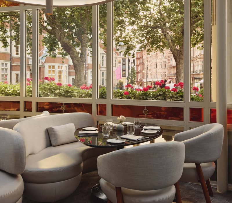 Elegant dining area with modern curved seating, stained glass windows, and a view of a vibrant, tree-lined street.