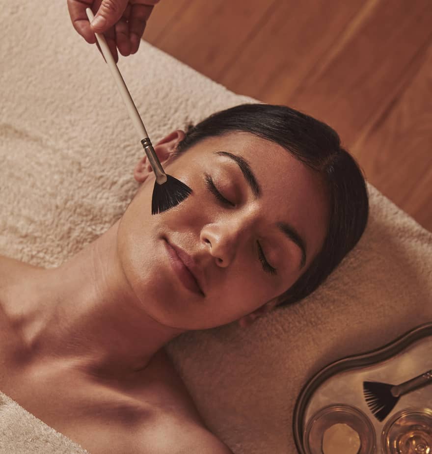 A serene moment of a woman receiving a luxurious facial treatment, as a gentle brush applies a soothing mask.