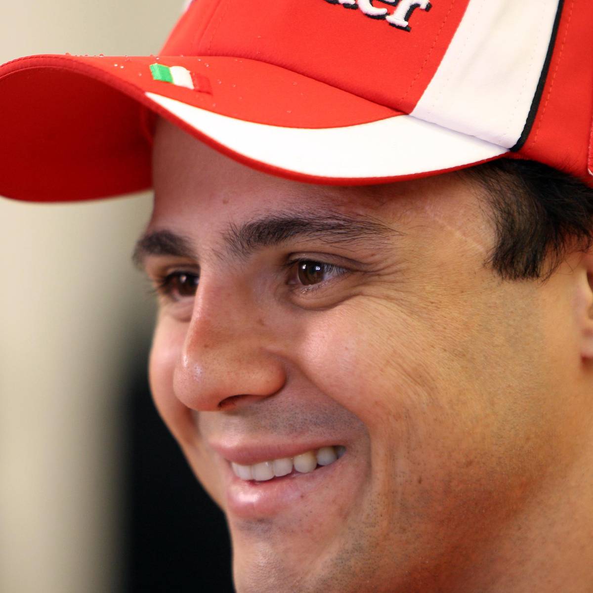 Smiling man in red Ferrari cap and team gear, close-up profile shot with blurred background.