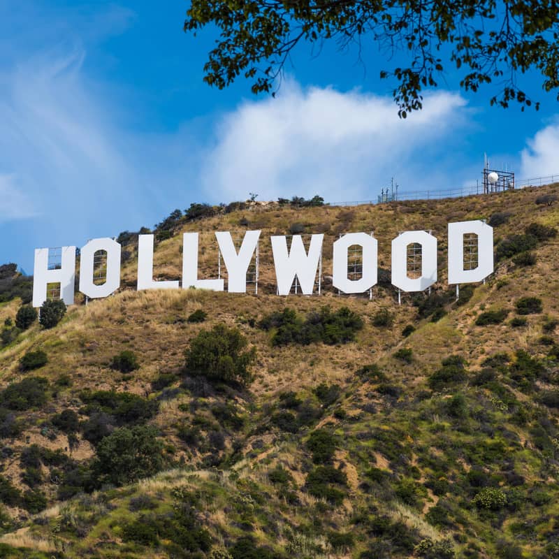 Iconic white Hollywood letters on a sunny hillside with blue sky and scattered clouds.