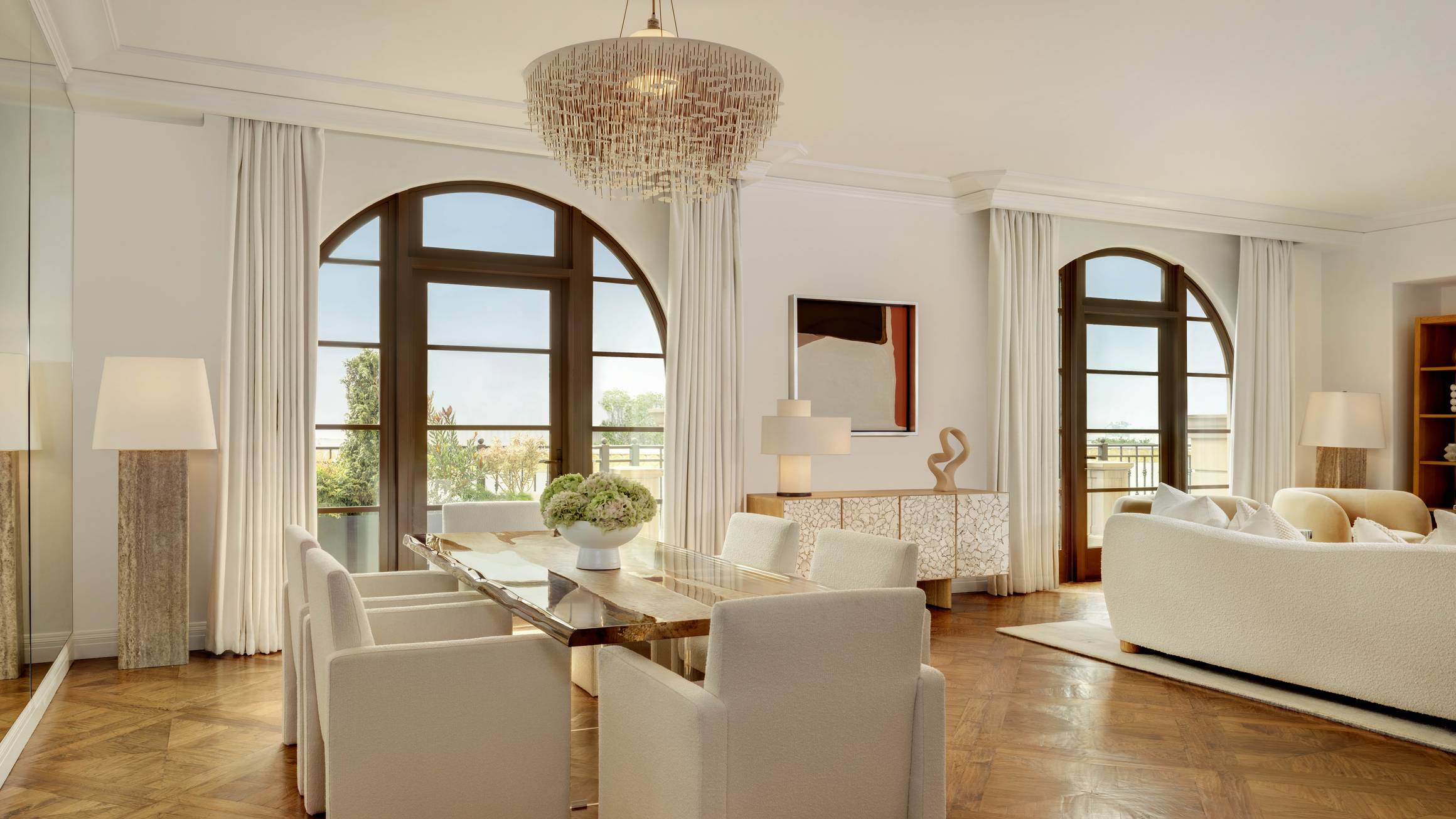 A refined open-plan dining and lounge area with arched windows, plush furnishings, and a statement chandelier, exuding modern sophistication.