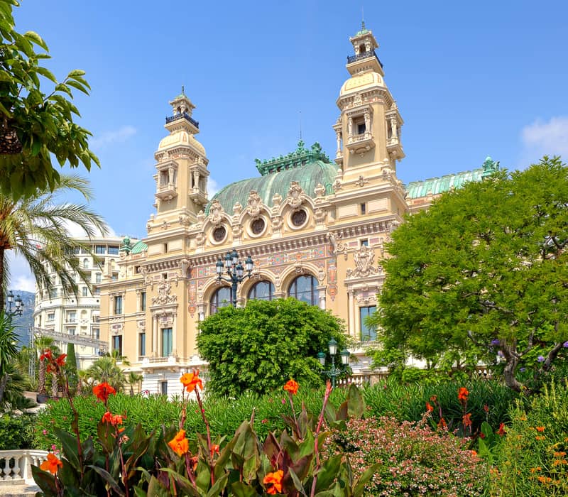 Magnificent opera house surrounded by lush gardens, showcasing its elegant architectural details under a deep blue sky.