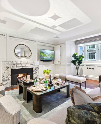 Elegant living room with marble fireplace, plush seating, coffee tables, and soft lighting beneath high ceilings.