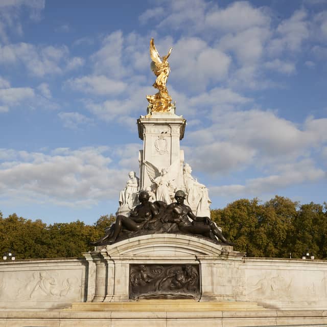 Majestic Victoria Memorial with golden statue and intricate sculptures, set against a backdrop of trees and blue sky.