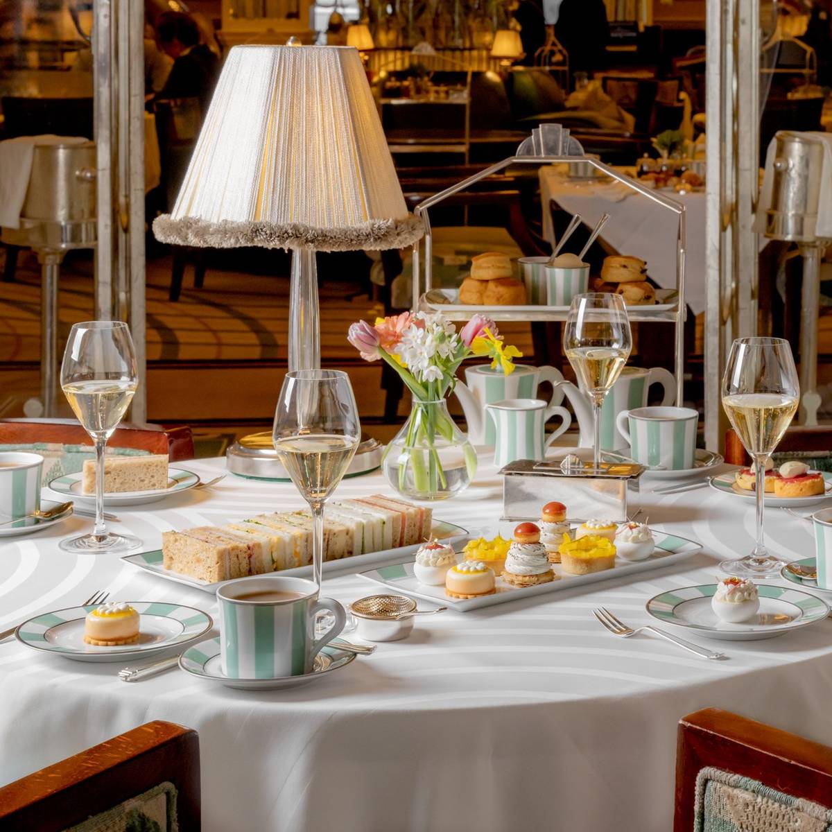 An elegant afternoon tea setting with fine china, delicate pastries, finger sandwiches, and champagne, exuding timeless sophistication and charm.