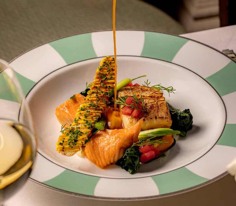 Exquisite grilled fish dish with fresh garnishes and a drizzle of velvety sauce, served on stylish striped dinnerware.