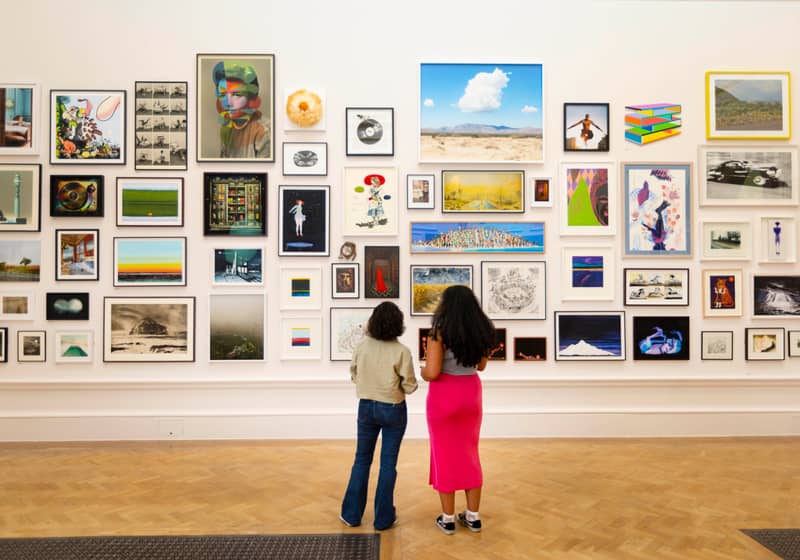 Two visitors admiring a striking wall of contemporary artworks in a prestigious London art exhibition.